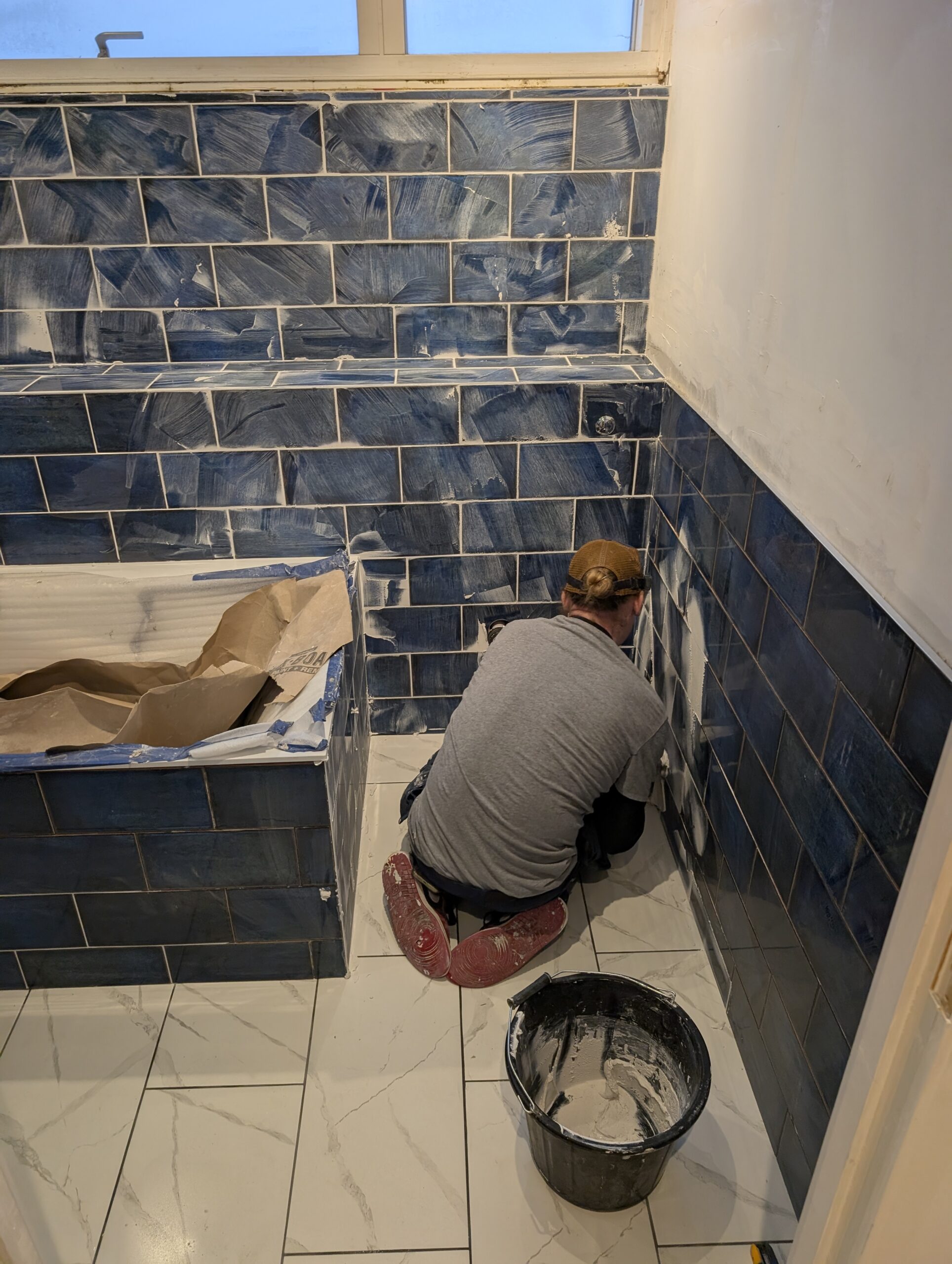 Man grouting blue subway tiles bathroom